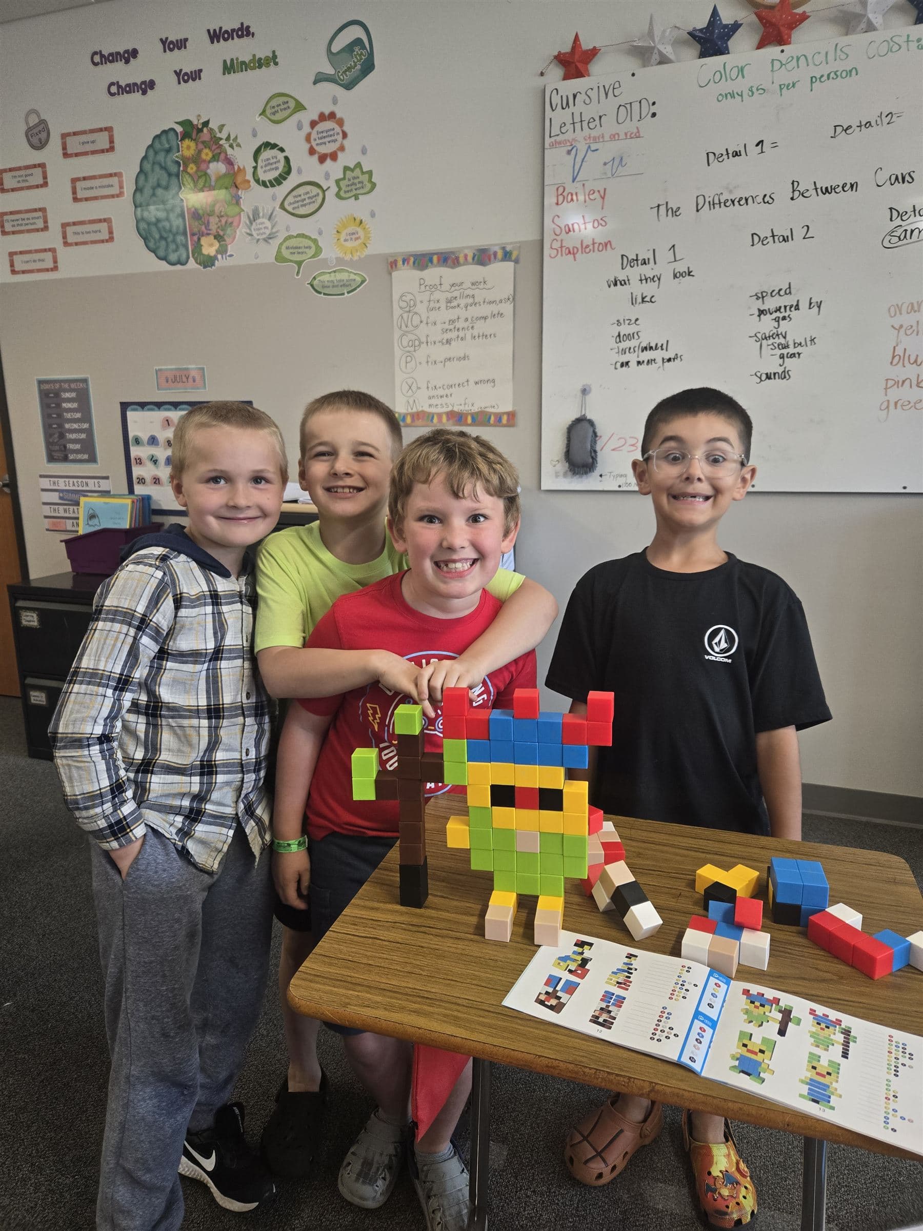 Four elementary students proudly showing a colorful block creature they built together