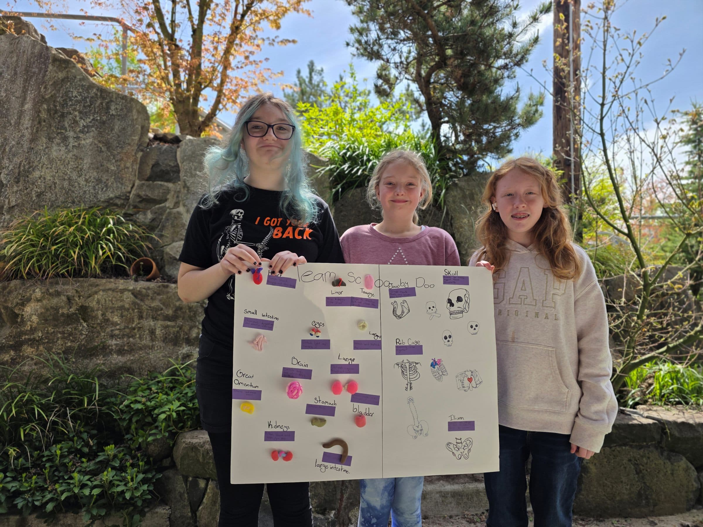 Three middle school students outside the school, proudly holding up the science project they made together