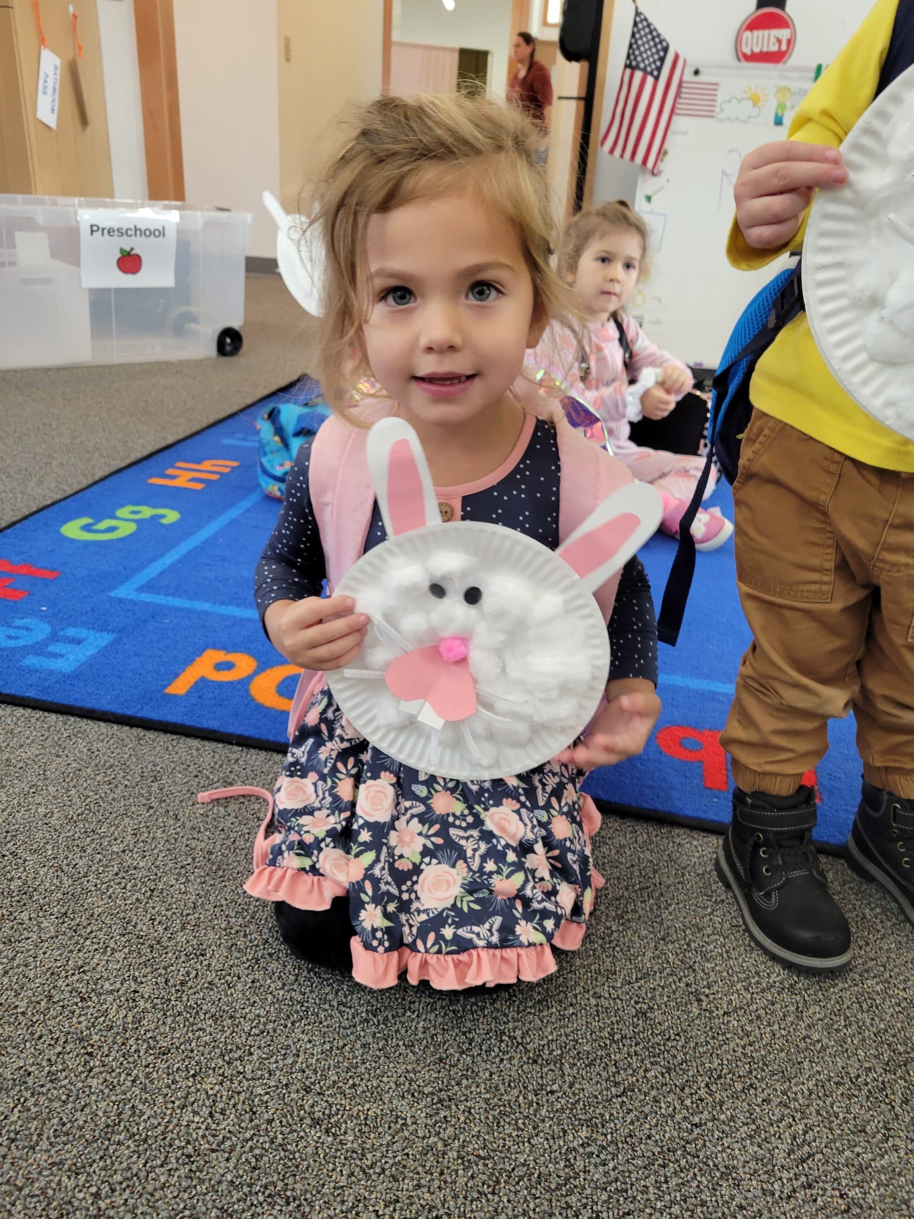 A young student proudly holding up the paper-plate bunny she made