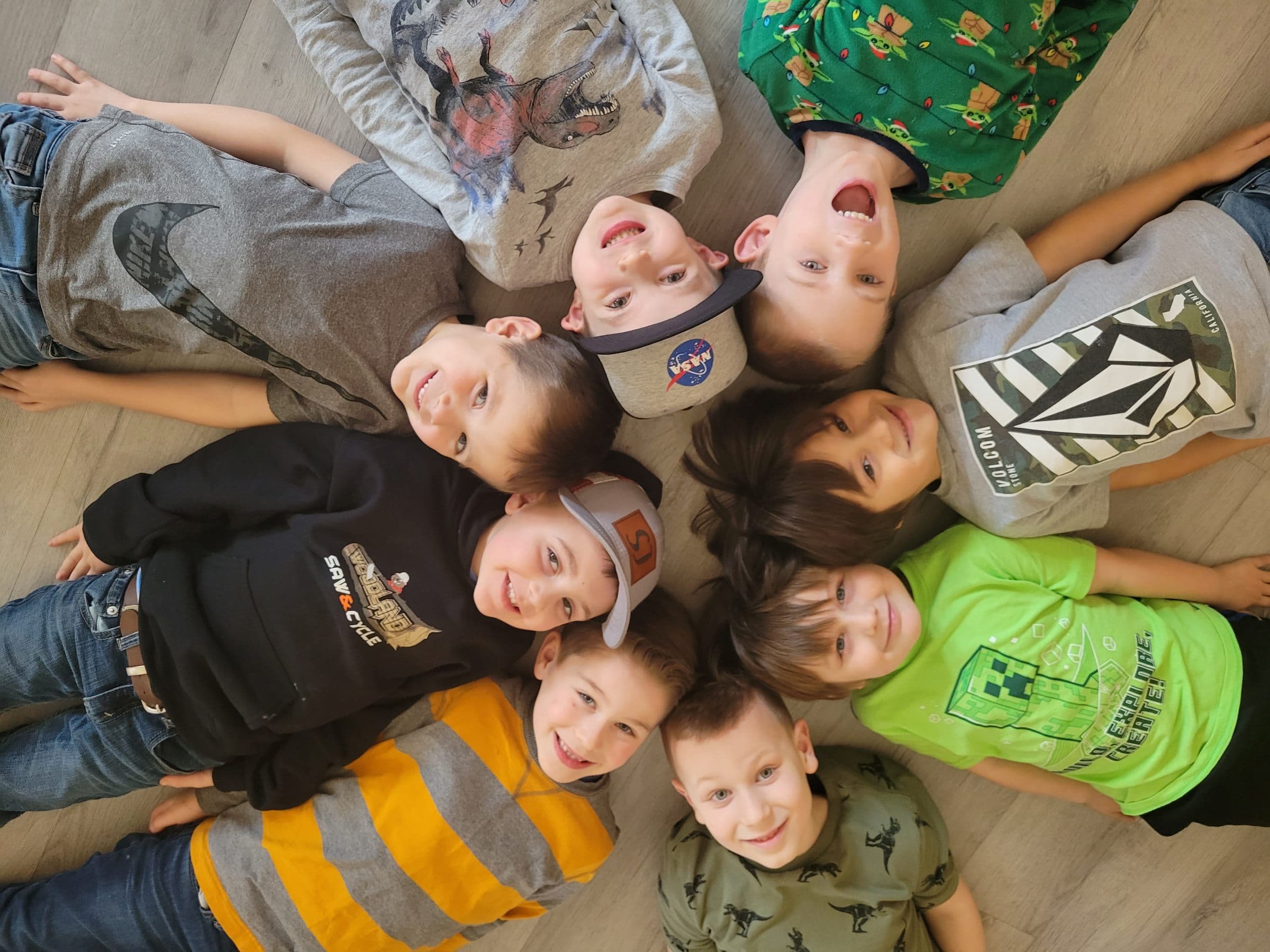 Classmates lying in a circle on the floor, heads together, all smiles