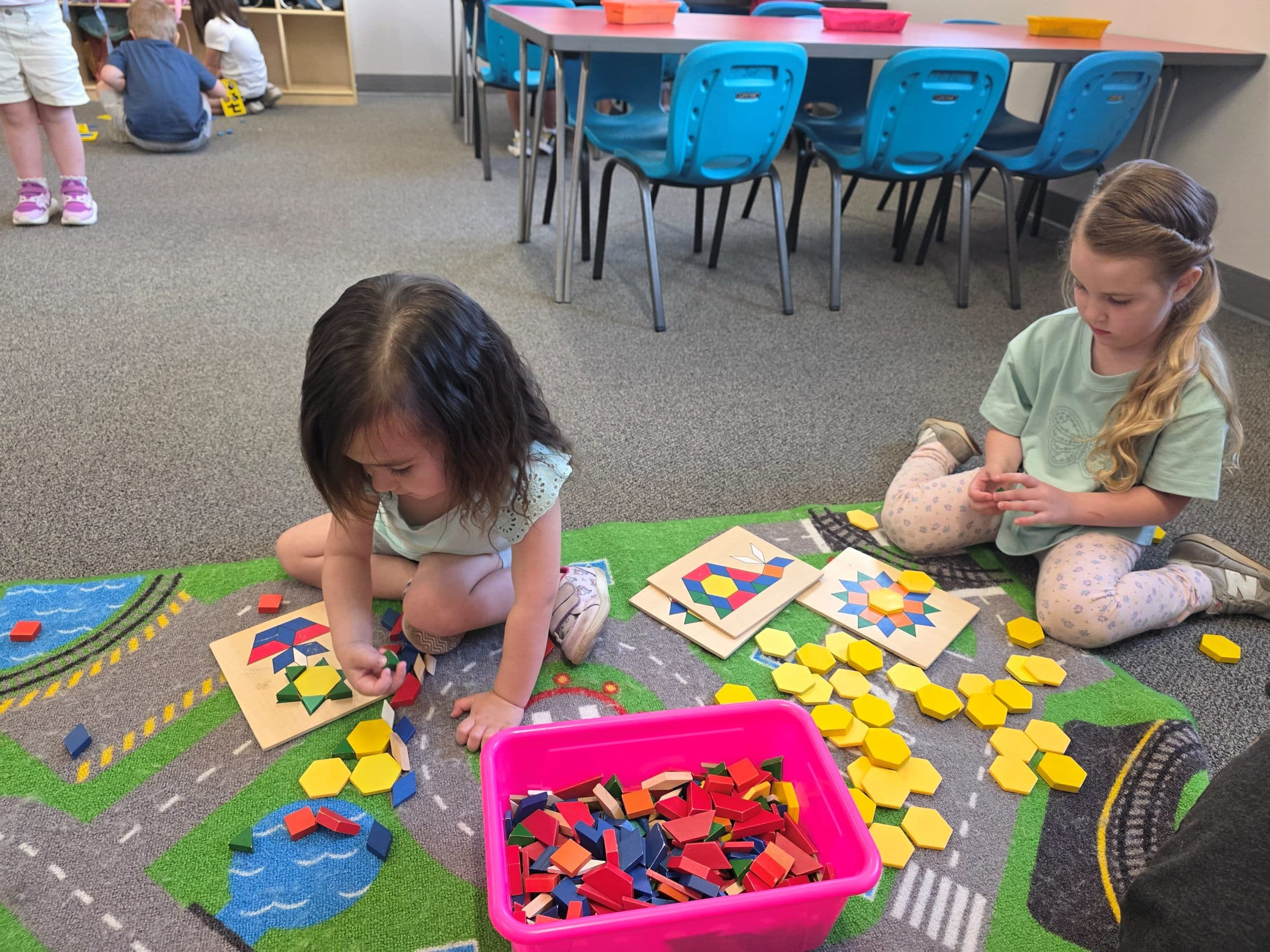 Two preschoolers building pattern-block designs on the classroom rug