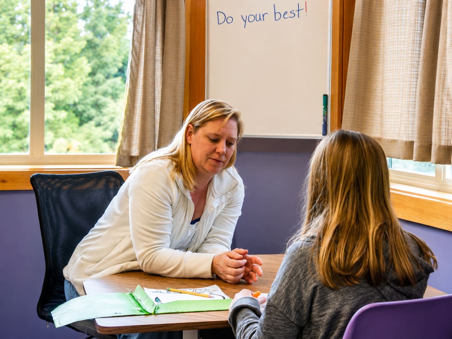 A tutor sitting one-on-one with a student, both writing together at a small desk